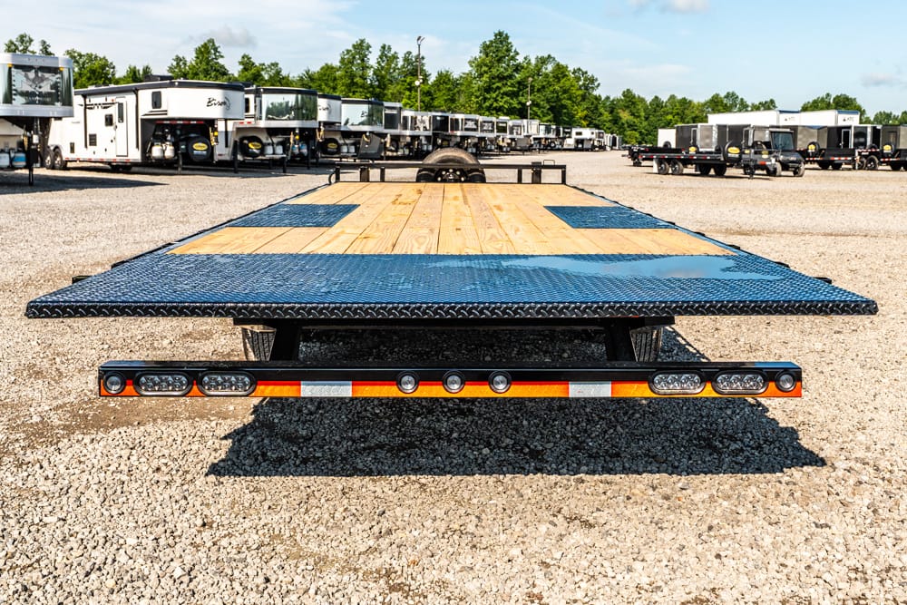 Low-angle view of a blue-and-wood flatbed trailer on a gravel lot, with a row of RVs in the background.