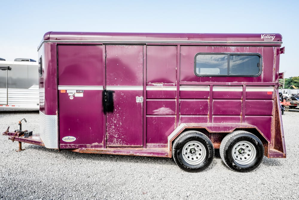 Purple horse trailer with two axles parked on gravel, side view showing doors and a window on the upper rear section