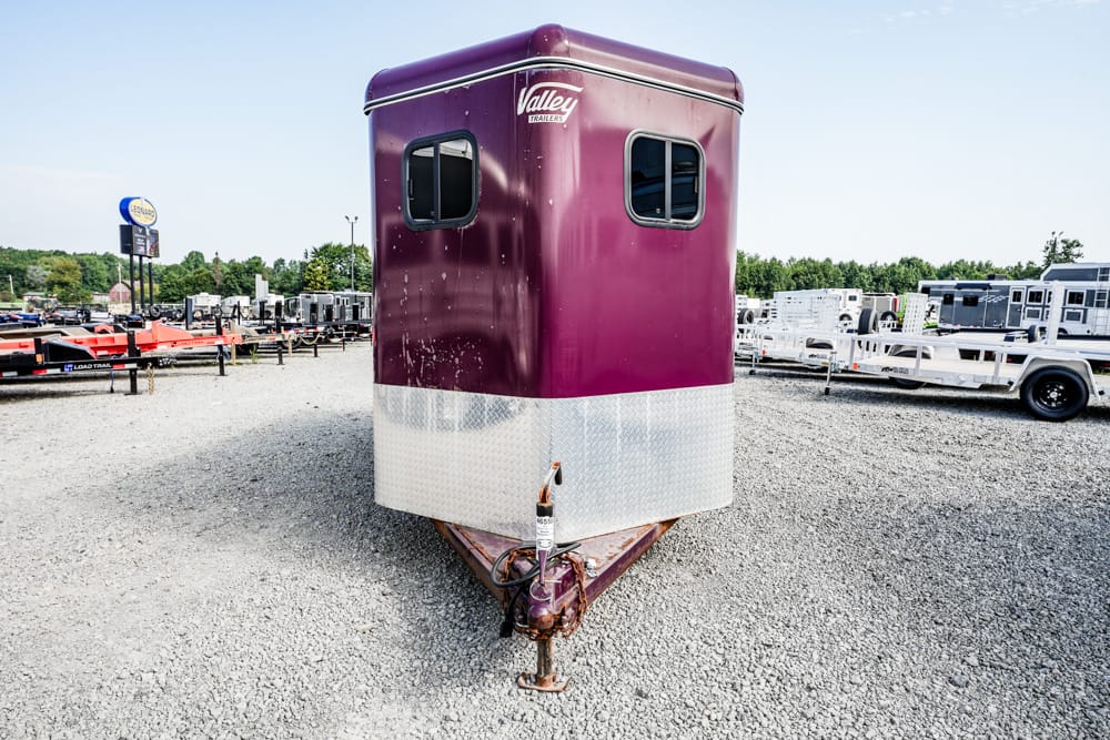 Front view of a maroon horse trailer with a silver bottom diamond plate on a gravel lot, other trailers in the background, Valley Trailers logo visible at the top front.
