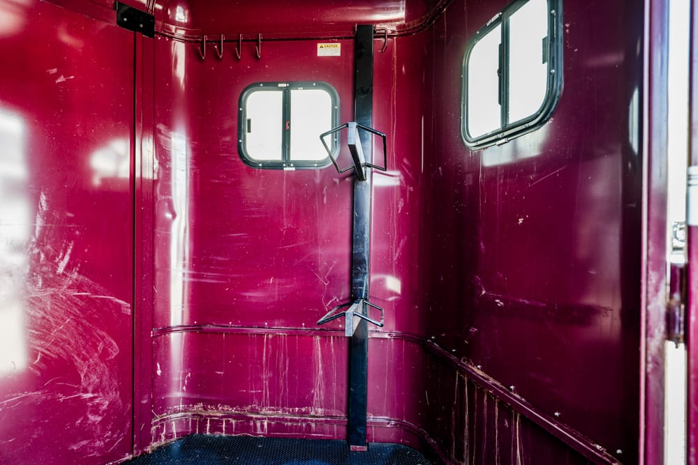 Interior of a maroon vehicle or trailer with a vertical black metal post and two mounting brackets, small oval windows on either side.
