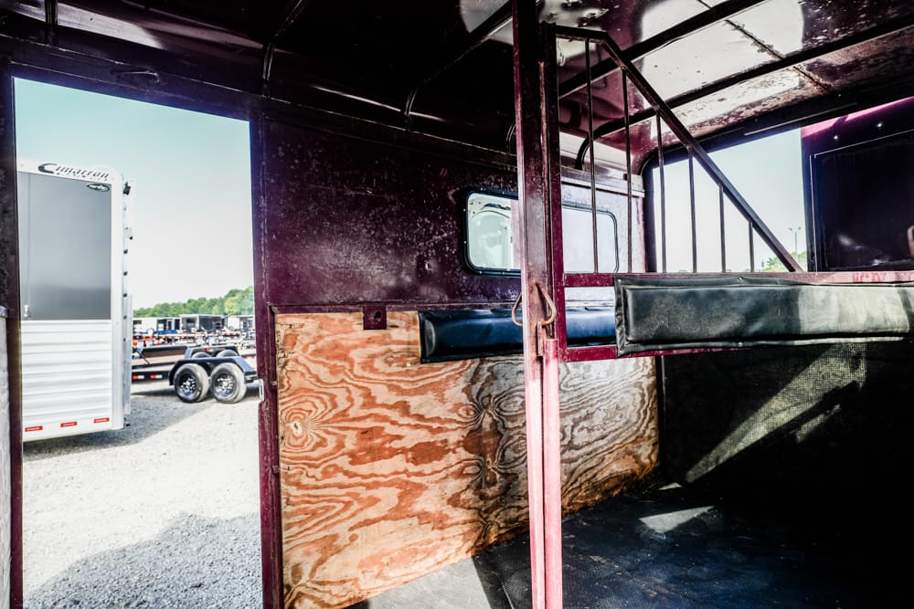 Interior of a dark maroon trailer with wood paneling and a padded partition; exterior trailers visible through the open door.