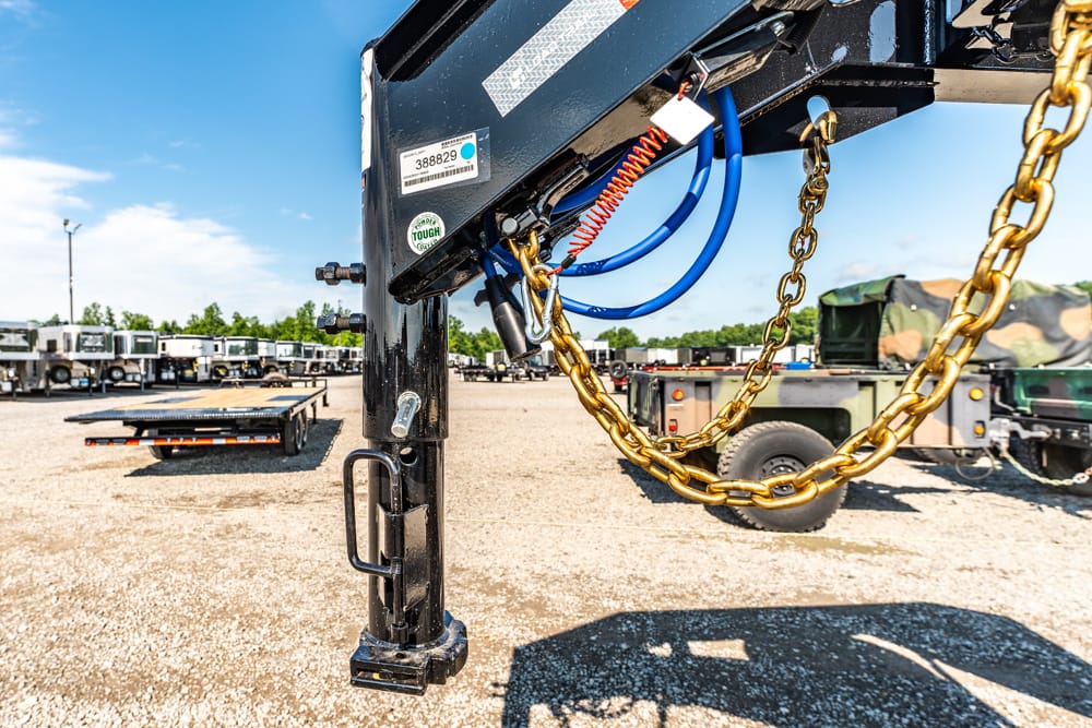 Close-up of a trailer hitch with a gold chain and blue air lines at a truck yard.