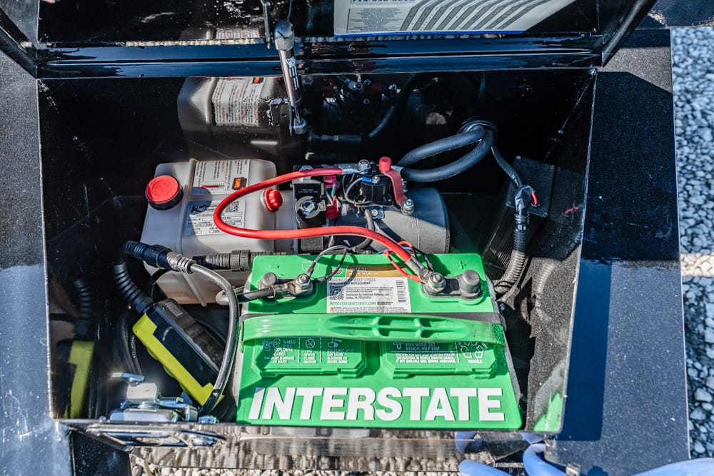 Green Interstate battery with red and black cables in a metal battery compartment.