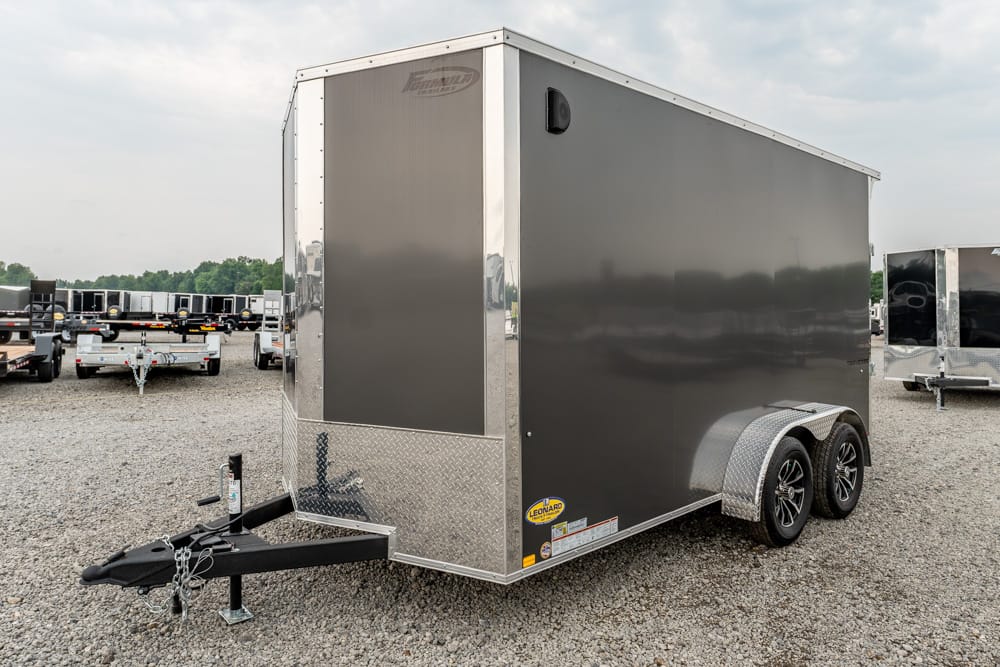 Dark gray, two-axle enclosed cargo trailer with diamond-plate front parked on a gravel lot among other trailers.