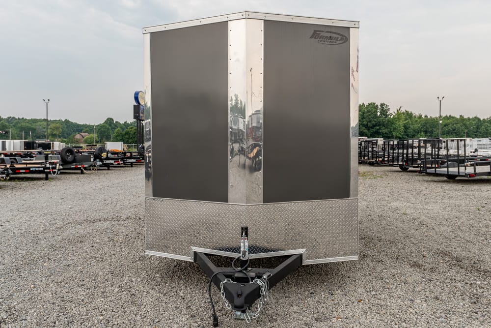 Front view of a tall enclosed cargo trailer with diamond plate at the lower front, hitch and safety chains showing, on a gravel lot.