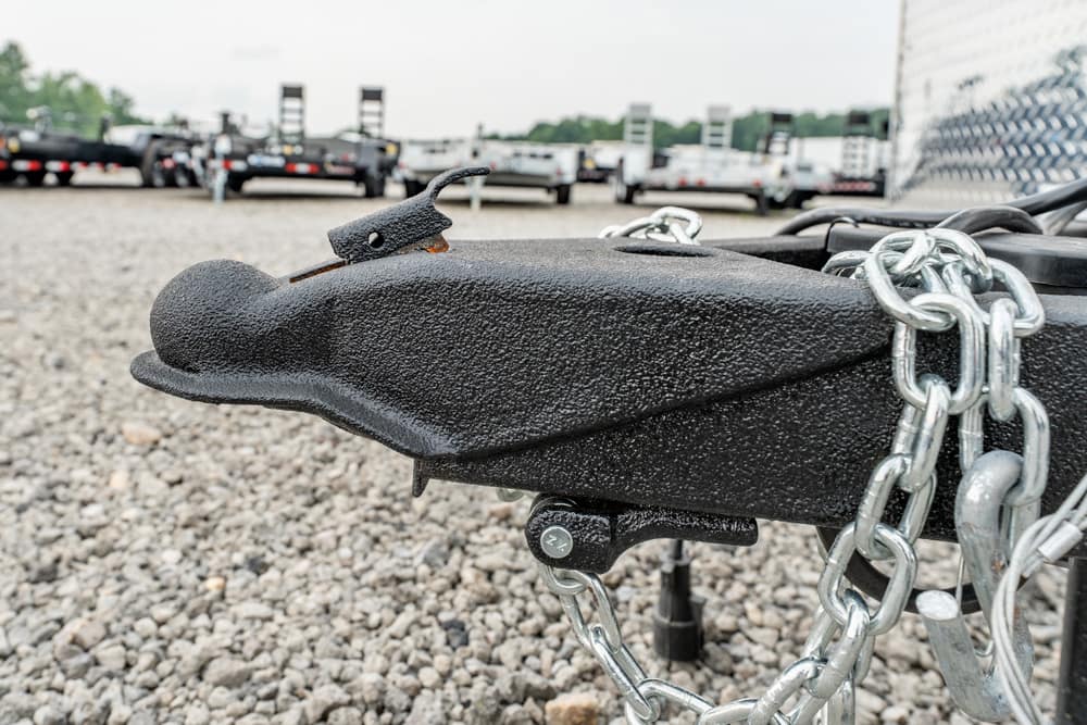 Close-up of a black trailer hitch with safety chains on a gravel surface, ready for towing.