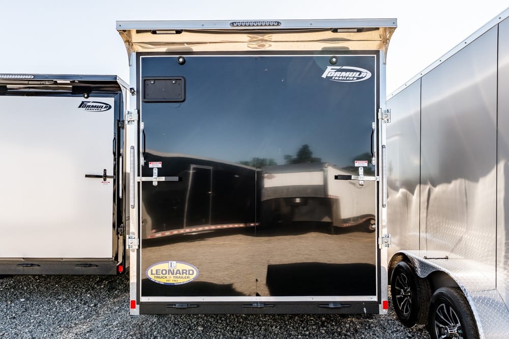Rear view of a black glossy enclosed cargo trailer with chrome trim, flanked by white and silver trailers; Leonard logo on bottom left corner.