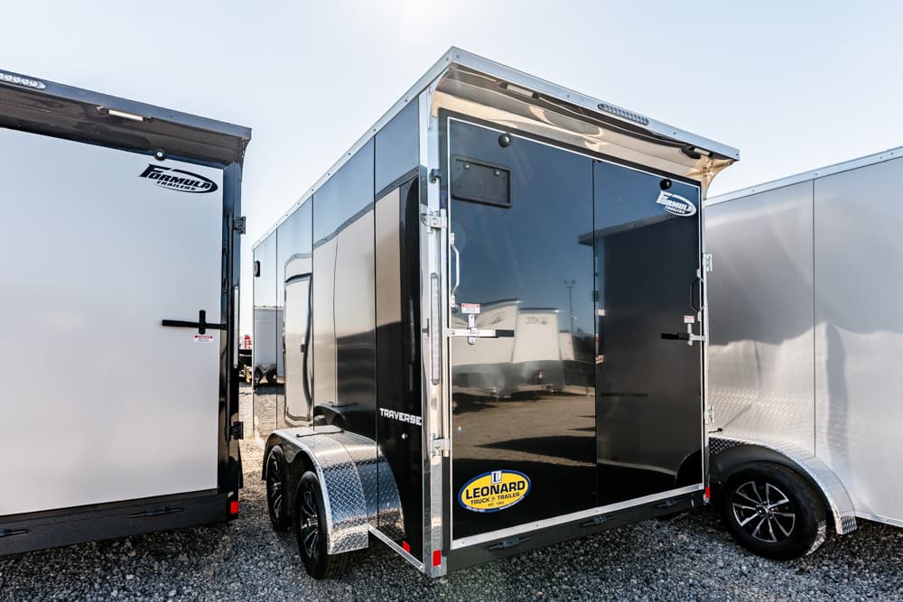 Black glossy enclosed cargo trailer with dual axles, parked between two other trailers, Leonard Truck & Trailer logo visible on the side.