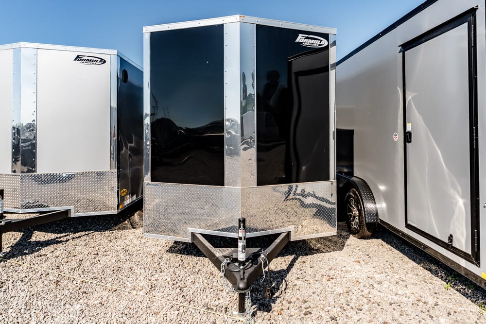 Three enclosed cargo trailers on a gravel lot with chrome diamond-plate fronts and a hitch in the foreground.