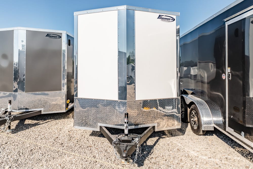 Three enclosed cargo trailers parked on gravel with chrome diamond plate trim and a front hitch.