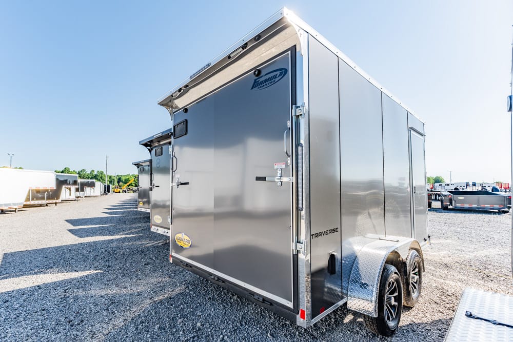 Shiny silver enclosed utility trailer with dual axles and diamond-plate fenders in a gravel lot.