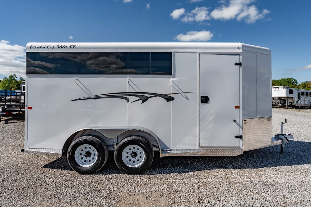 White enclosed horse trailer with black abstract graphics and dual axles on a gravel lot under a blue sky.
