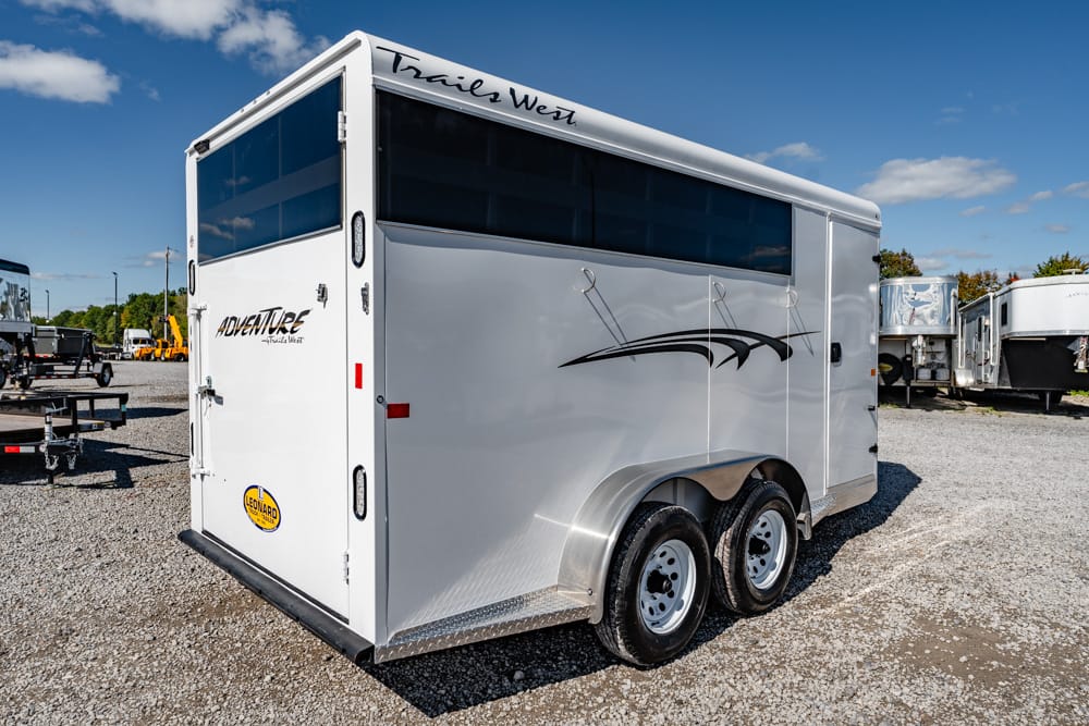 White Trails West horse trailer with two axles parked on a gravel lot, featuring dark-tinted windows and decorative graphics on the side.
