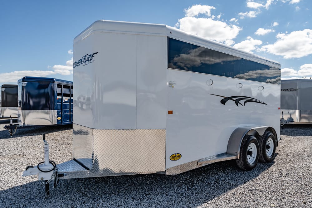 White enclosed cargo trailer with diamond-plate front on a gravel lot, two axles visible.
