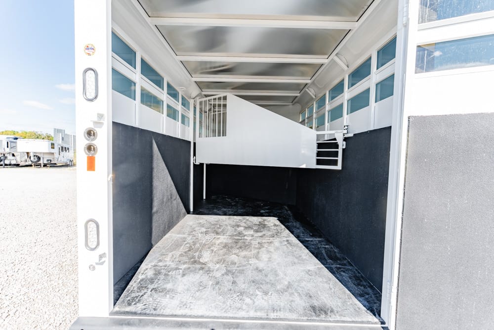 Empty horse trailer interior with a white divider and ramp, black lower walls, and windows along the sides