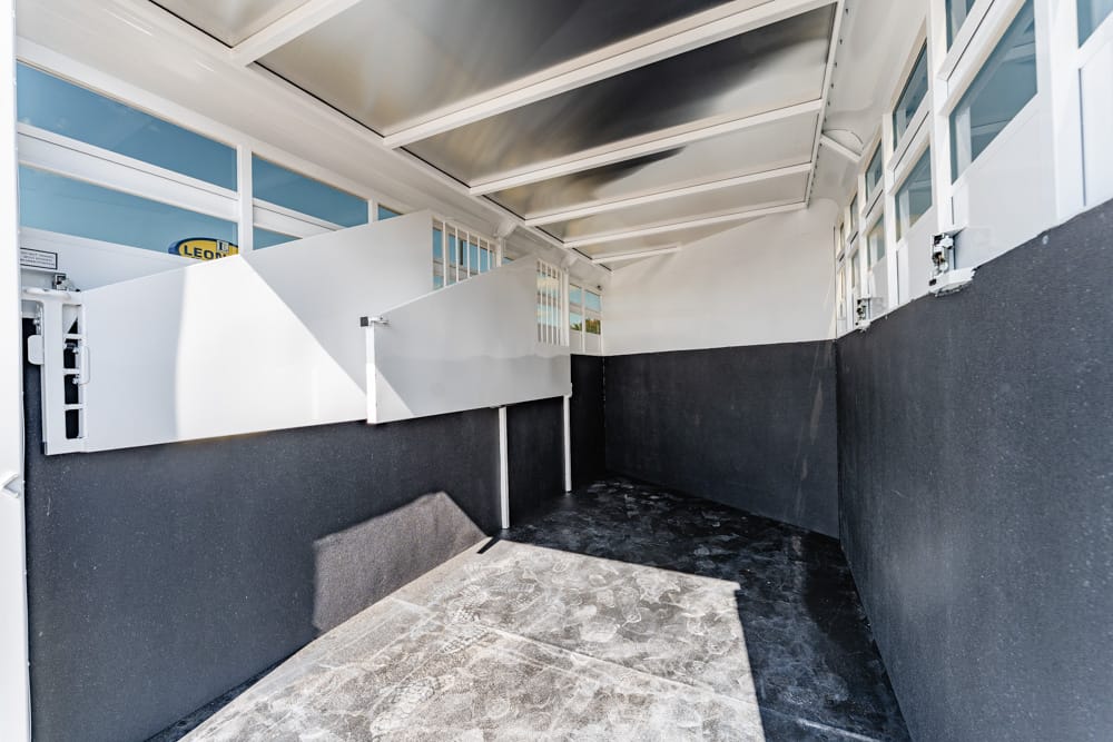 Interior of a loading trailer with white partition panels and dark lower walls, empty and well-lit by skylights.