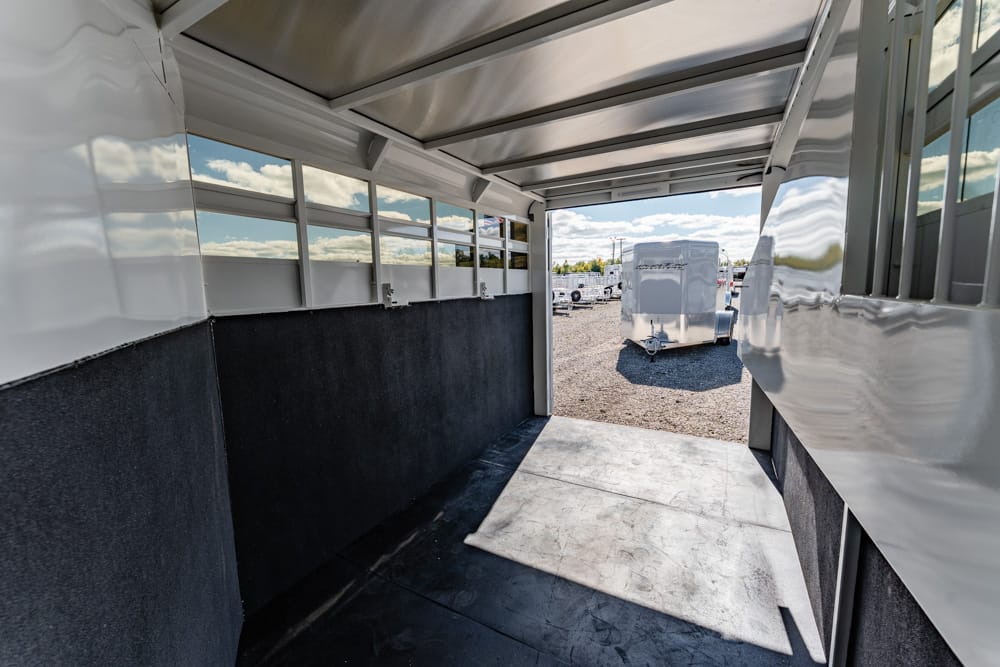 Interior of an empty aluminum trailer with open back ramp, exposing a gravel lot and parked trailers outside at a trailer park