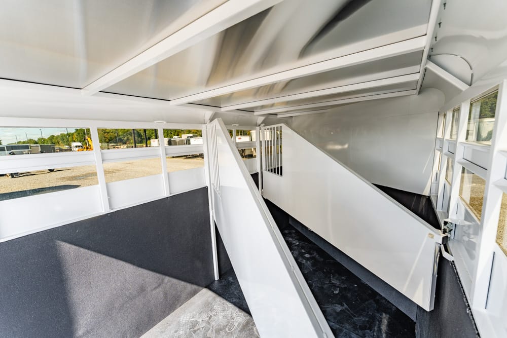Interior of a white horse trailer with partition gates and a narrow central aisle, empty and ready for loading animals.