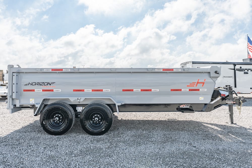 Gray Horizon dump trailer with dual axles on a gravel lot under a blue sky, ready for transport.