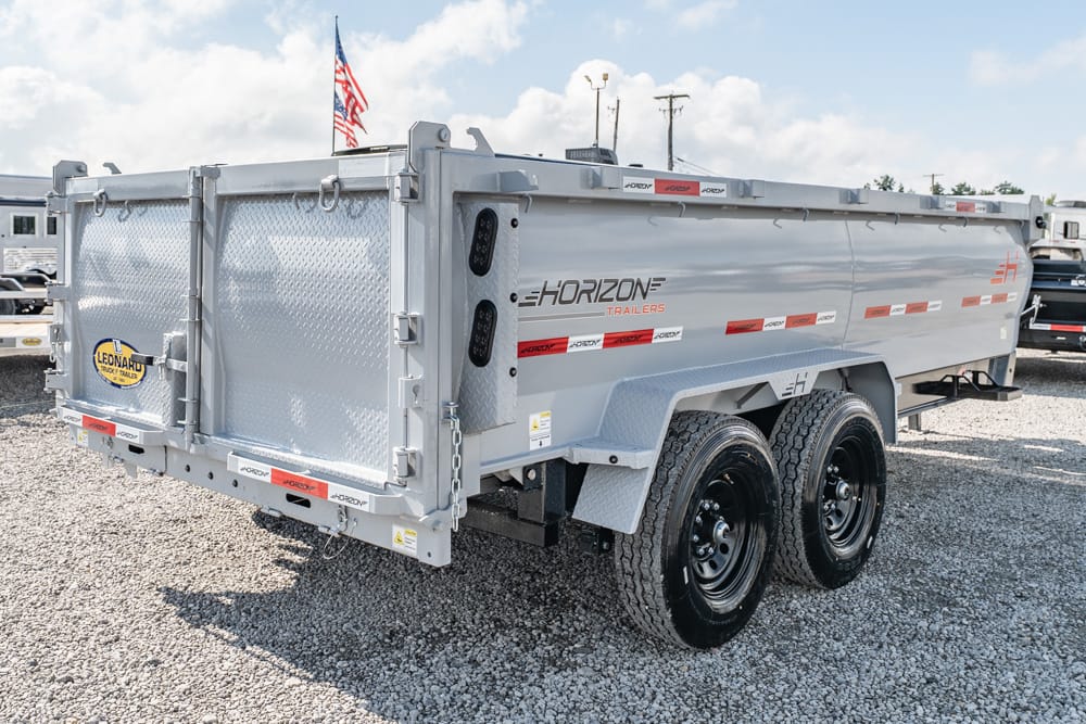 Dual-axle silver Horizon dump trailer parked on a gravel lot with diamond-plate sides and red safety tape