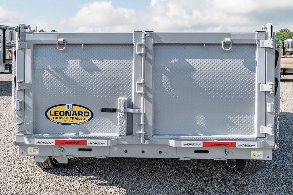 Rear view of a silver dump trailer with diamond-plate doors and the Leonard logo on gravel.