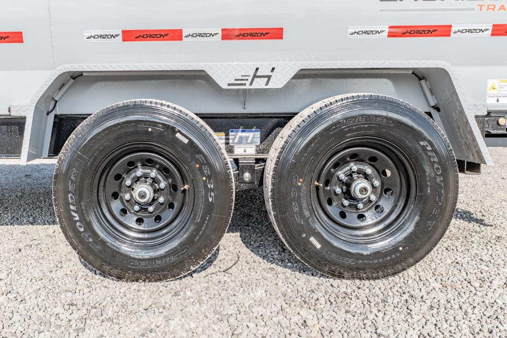Dual black wheels of a cargo trailer on gravel, with a grey fender and Horizon branding visible on the trailer