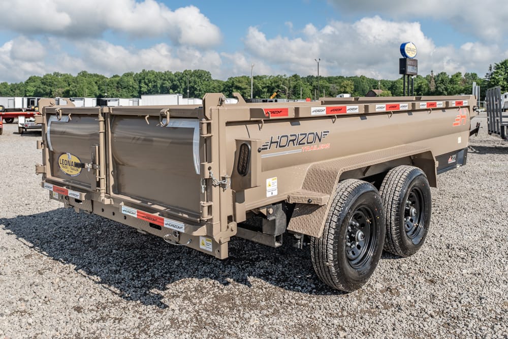Tan Horizon dual-axle dump trailer parked on a gravel lot with a closed rear gate under a blue sky with clouds.