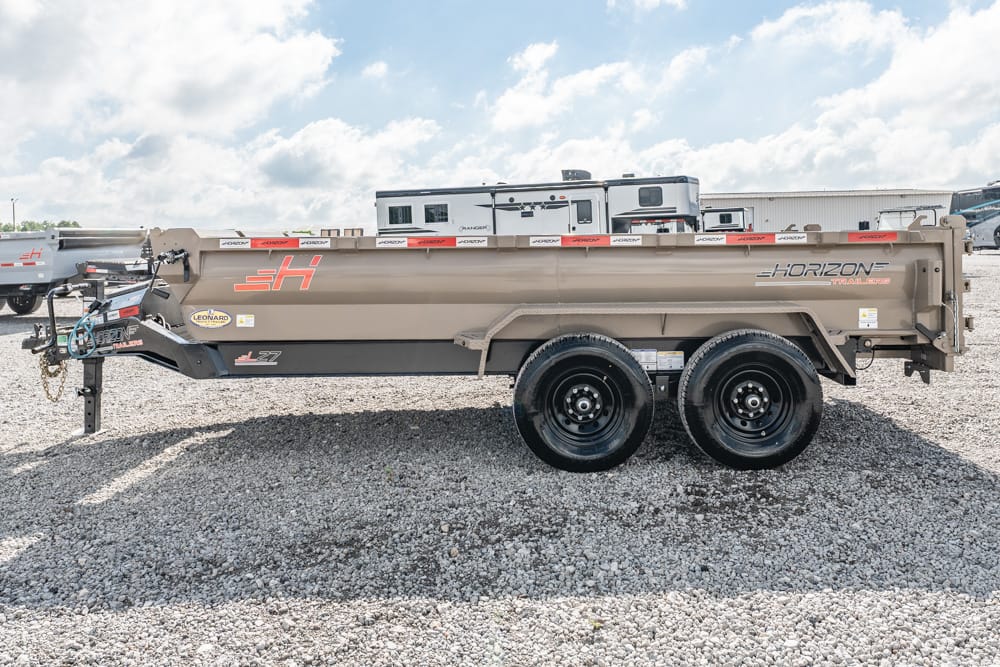 Tan Horizon dump trailer with dual axles, hitch connected, parked on a gravel lot by a storage area.