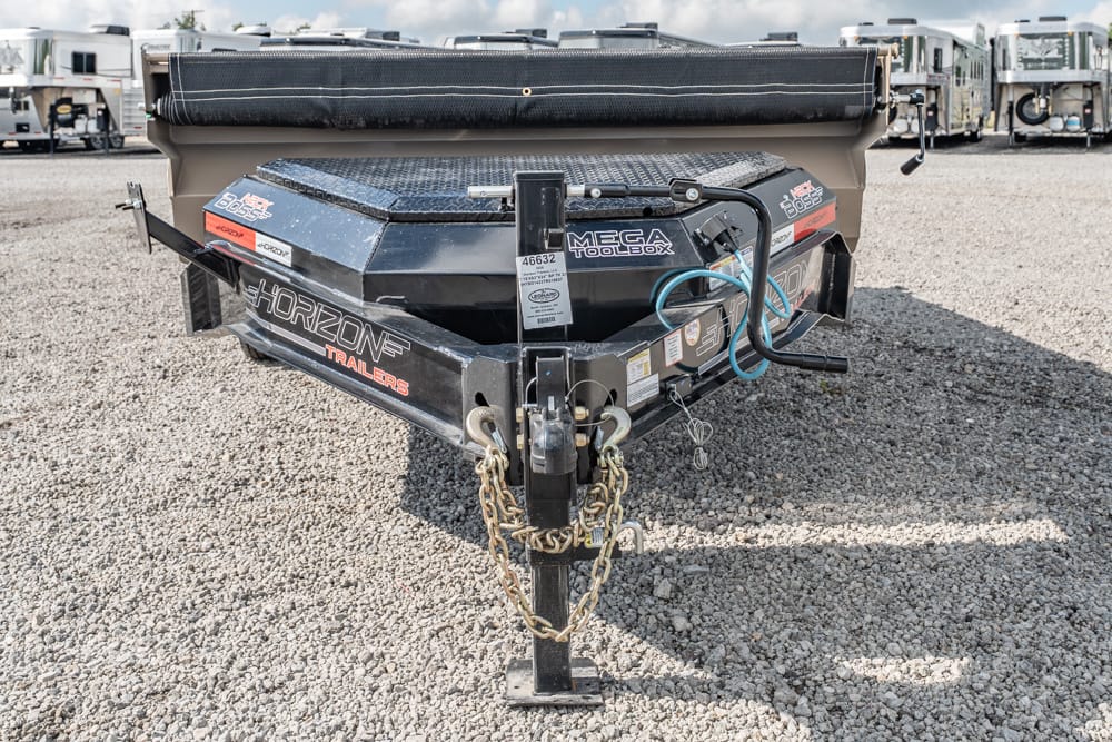 Front view of a Horizon Trailers trailer tongue with a diamond-plate toolbox, safety chains, and hitch on a gravel lot in front of RVs.