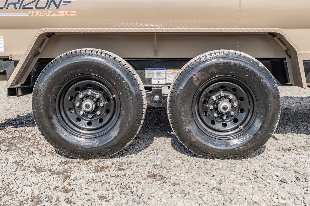 Dual-axle trailer with black steel wheels and beige body on a gravel surface.