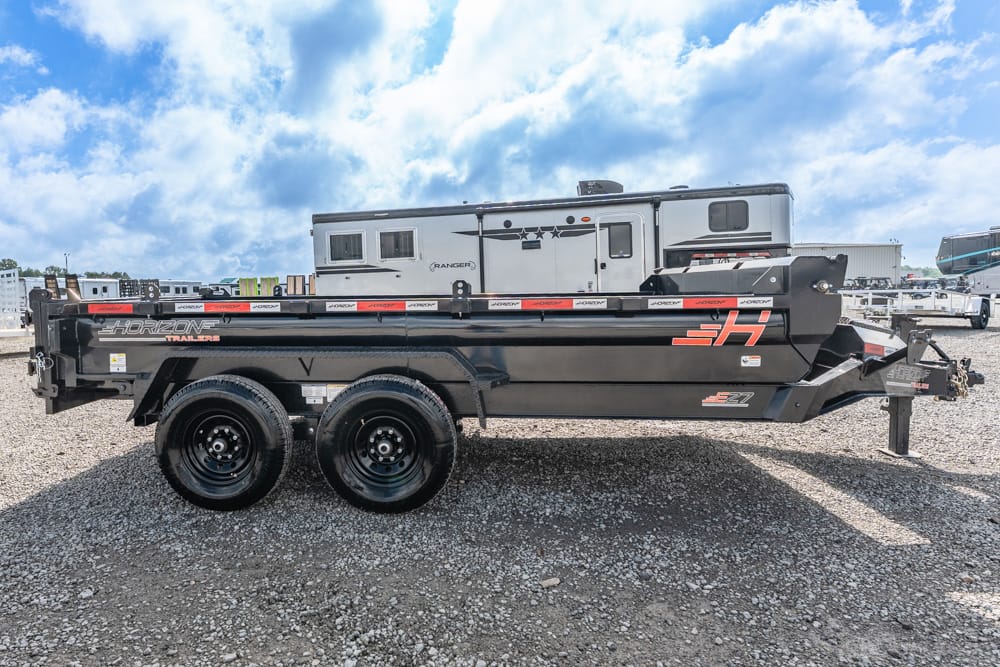 Black Horizon tandem-axle utility trailer on a gravel lot with an RV in the background, ready for use.