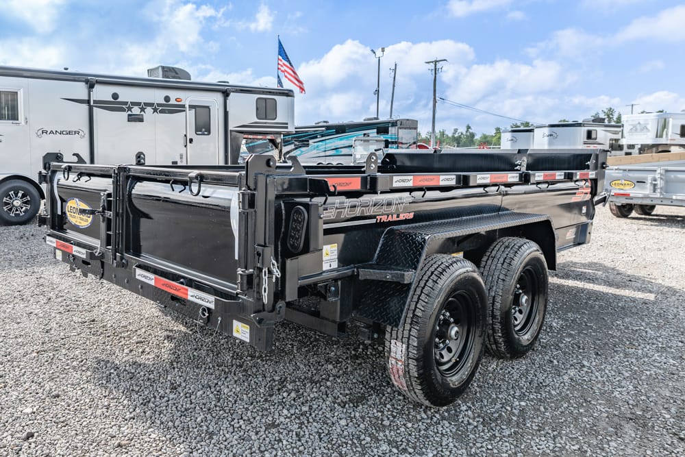 Black Horizon dump trailer with dual rear wheels parked on a gravel lot, with RVs in the background and an American flag on a nearby trailer