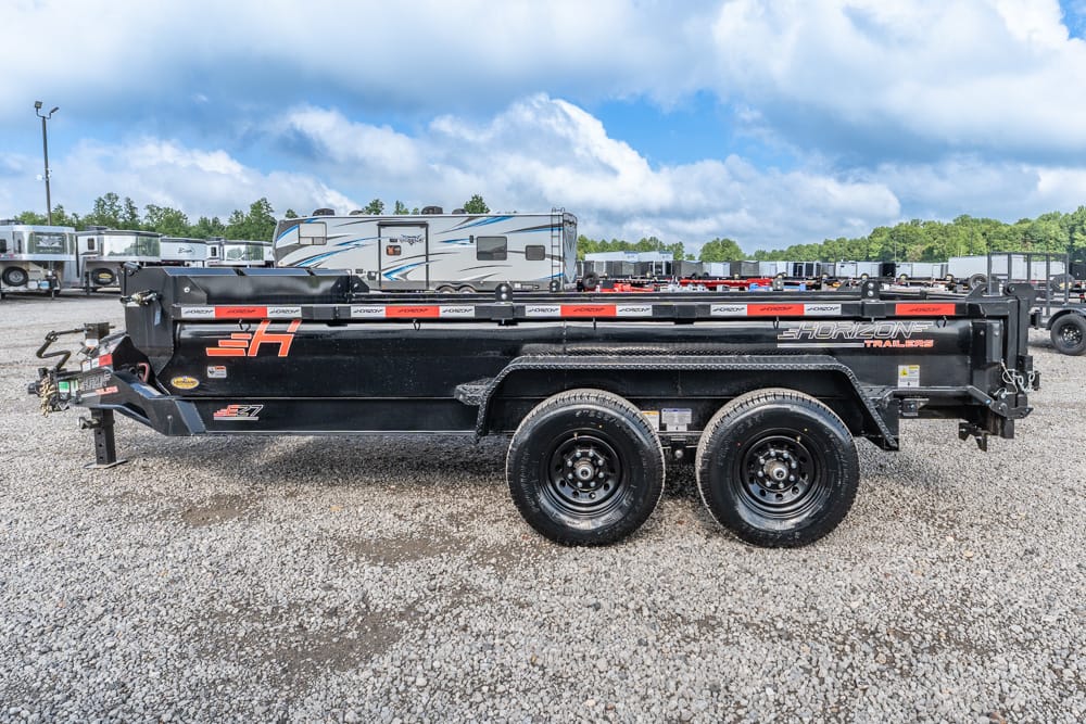 Side view of a black dual-axle Horizon dump trailer with orange graphics parked on a gravel lot. The Horizon Trailers logo is visible on the side.