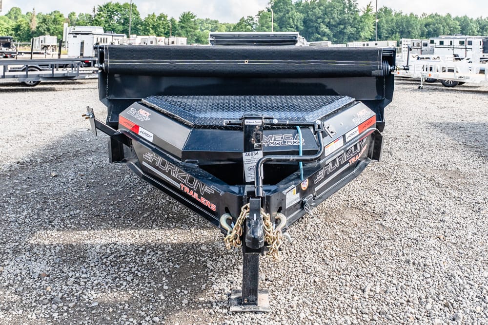 Black utility trailer hitch and toolbox on a heavy-duty trailer in a gravel lot with other trailers in the background. Details include Horizon Trailers branding and a diamond plate surface.