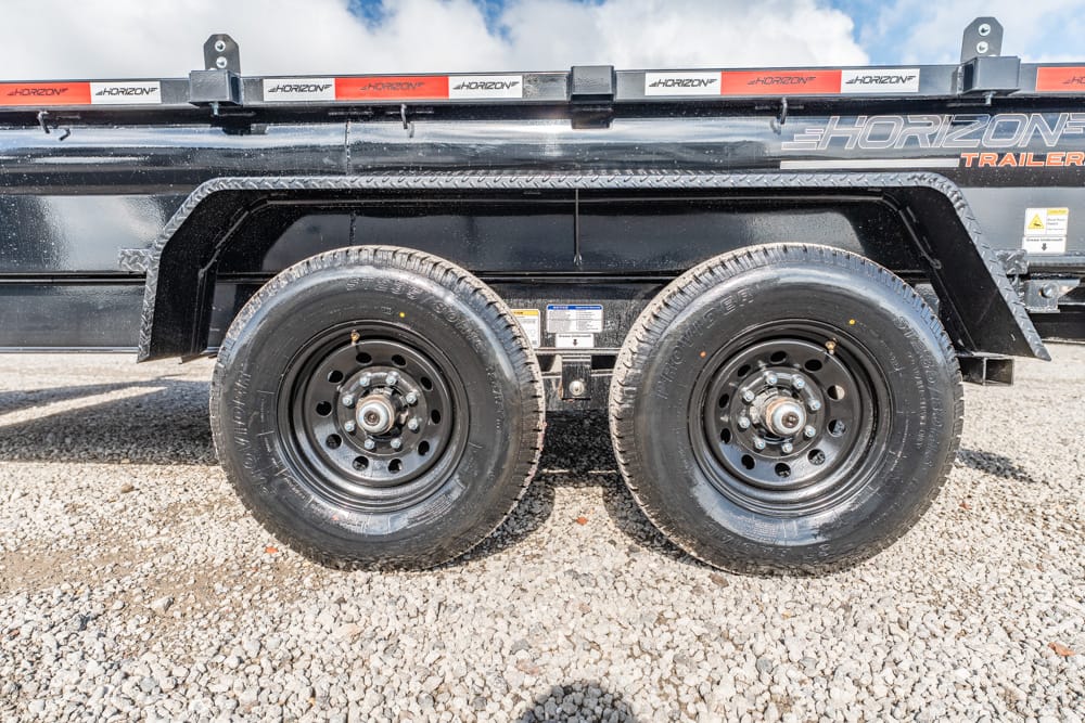 Dual-axle utility trailer with black rims and large tires, parked on gravel, Horizon branding along the side.