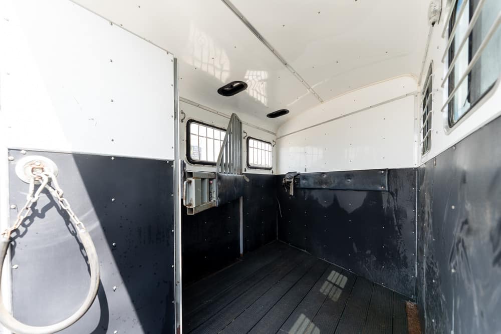 Interior of an empty horse trailer with white upper walls, black lower panels, and a ribbed rubber floor.