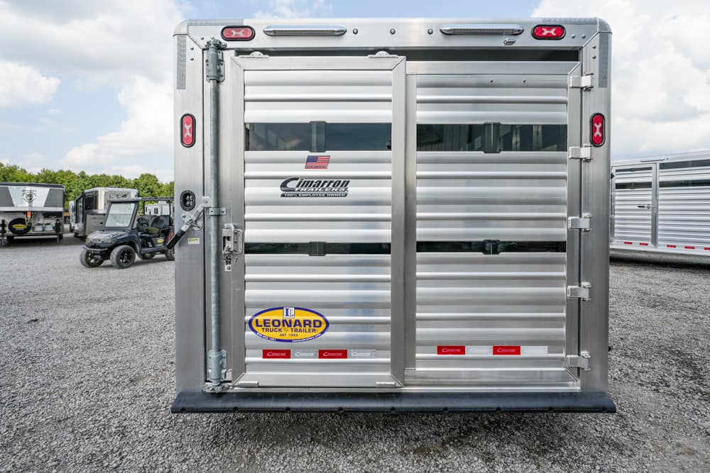 Rear view of a silver aluminum trailer with double doors and latch hardware, showing brand stickers (Leonard) and (Cimarron).