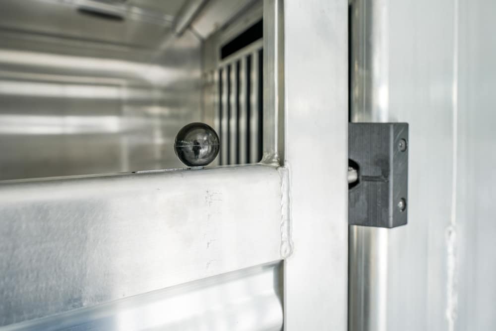 Close-up of a black knob resting on a stainless steel door edge in an industrial cabinet/rail system.