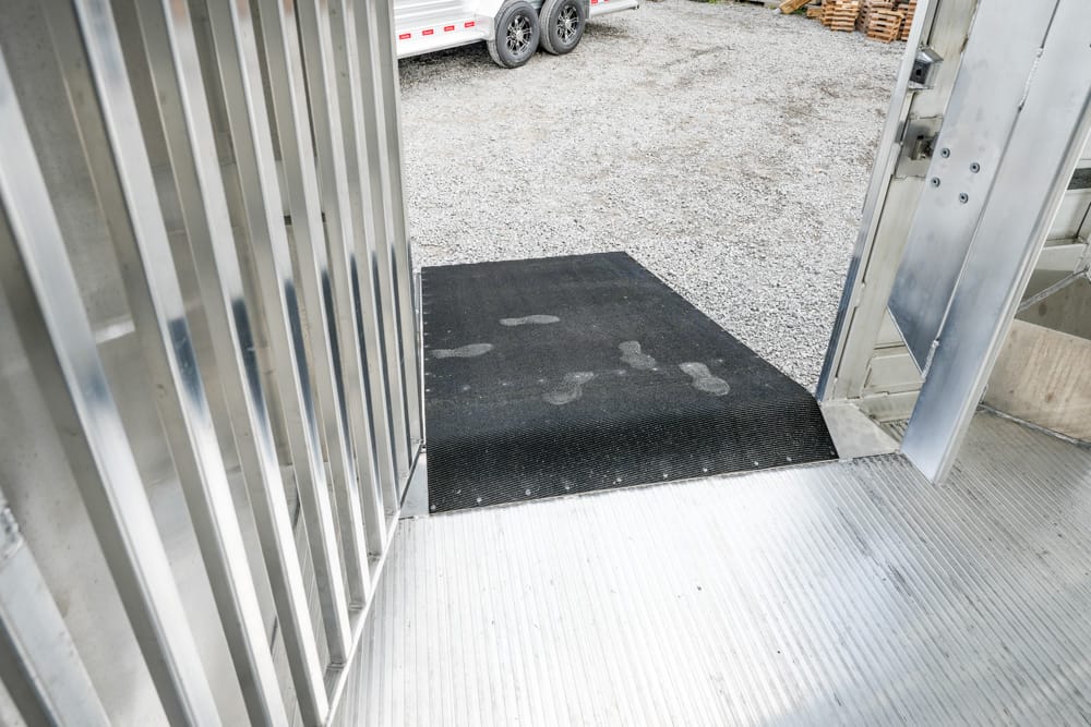 Open trailer doorway with a black rubber ramp mat at the threshold leading to a gravel yard outside.