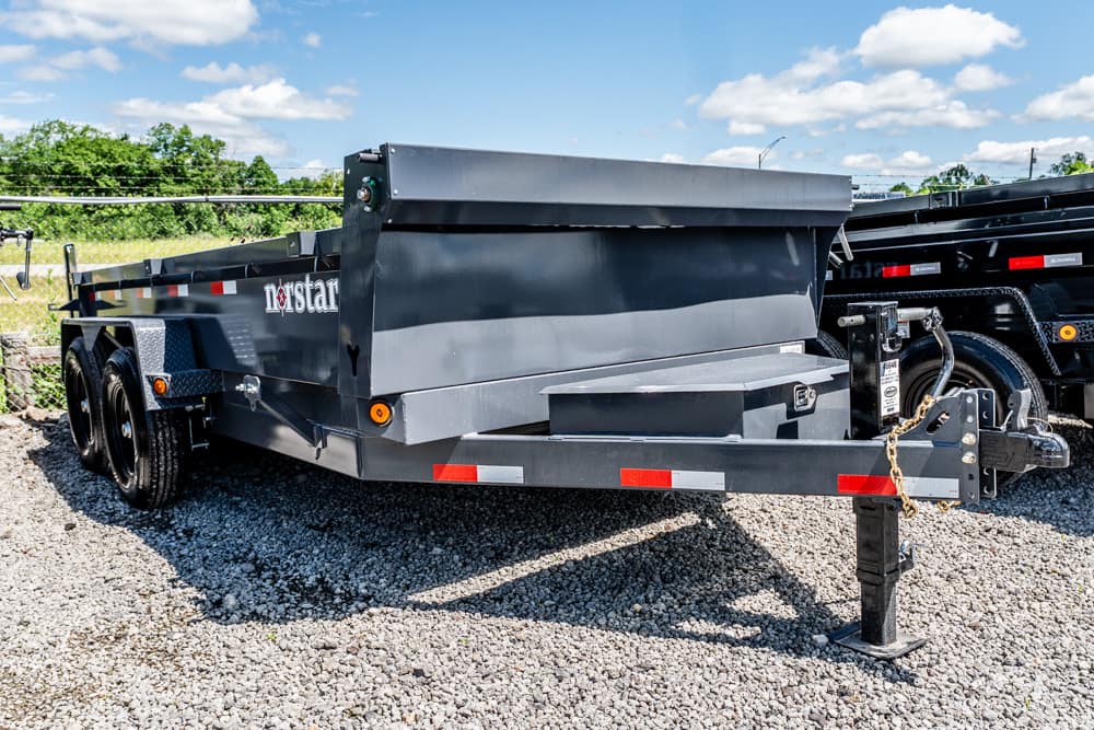 Grey Norstar dump trailer on a gravel lot, showing dual rear wheels and folded tailgate for loading and transport of materials.