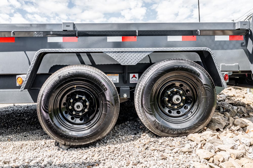 Dual black trailer wheels on a gray dump trailer resting on gravel ground