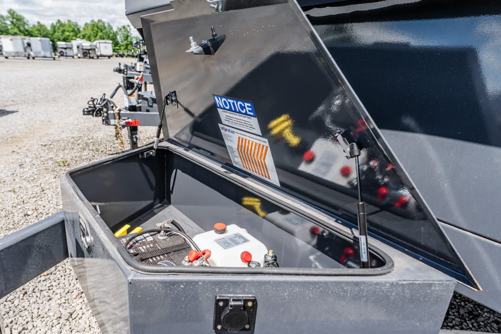 Open trailer storage box showing a battery and wiring inside, with a Notice sticker on the lid