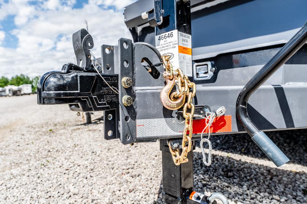 Trailer hitch secured with a gold chain and two padlocks on a parked gray trailer.