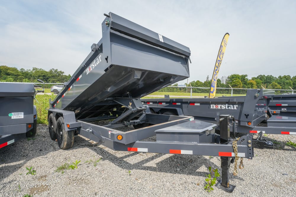 Gray Norstar dump trailer with raised bed in a gravel lot, ready to unload.