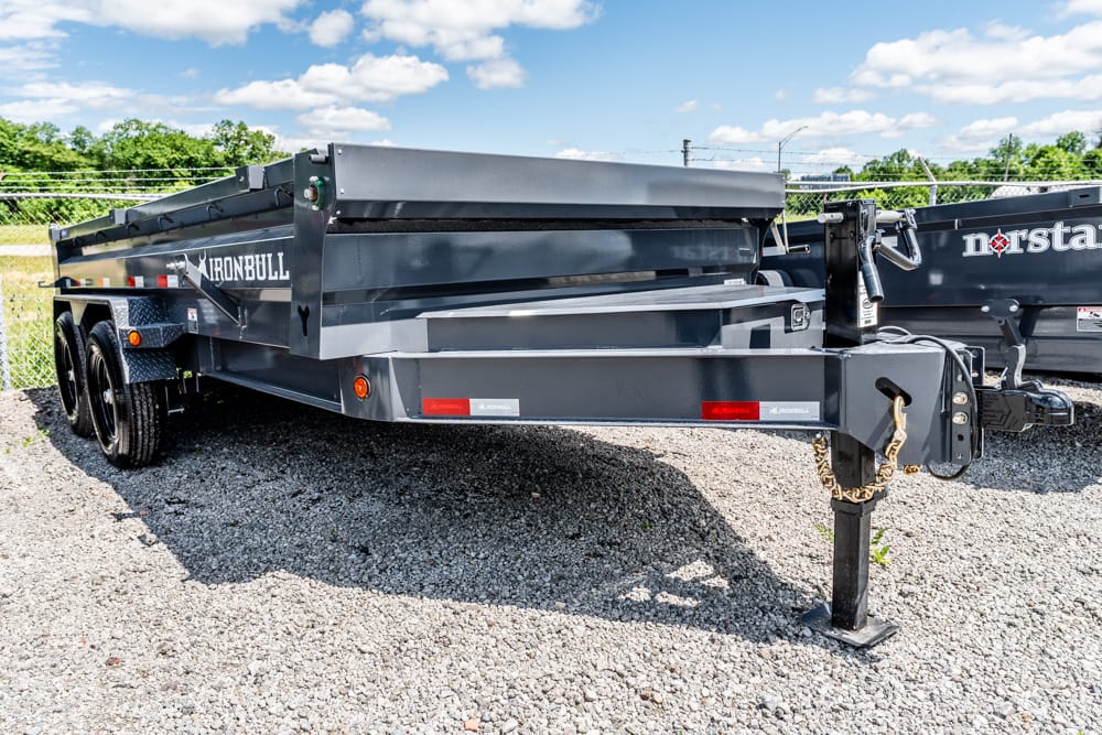 Gray dual-axle dump trailer on a gravel lot, hitch and safety chain visible, Iron Bull branding on the side.