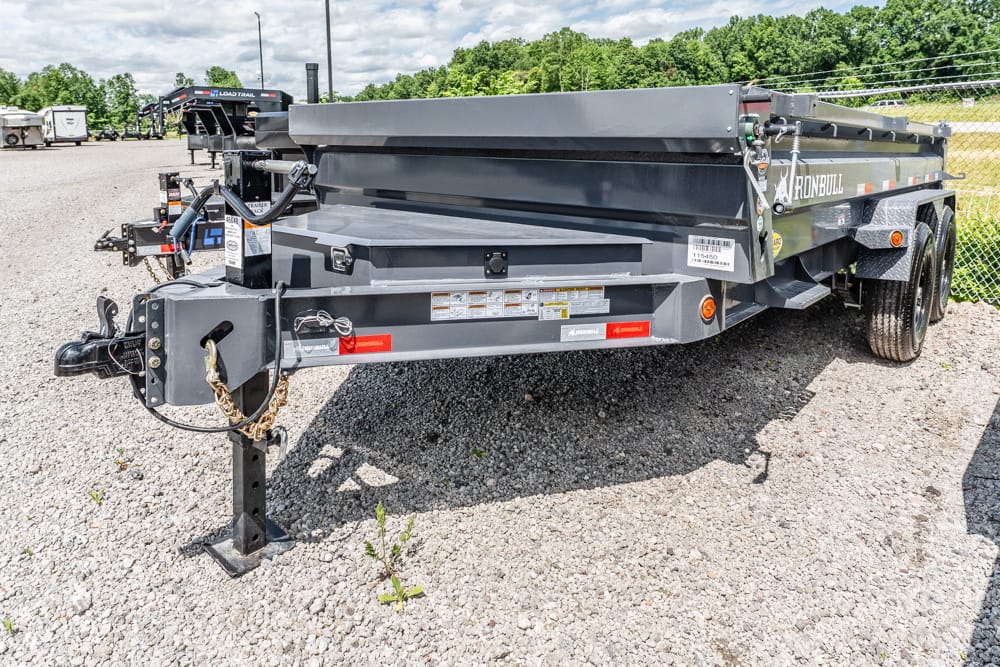 Iron Bull dual-axle gray dump trailer on a gravel lot with hitch, jack stand, and safety chains in view