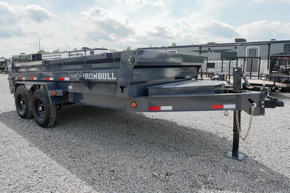 Gray Ironbull dump trailer with tandem axles on a gravel lot, front hitch with safety chains visible, RVs in the background (informational image).