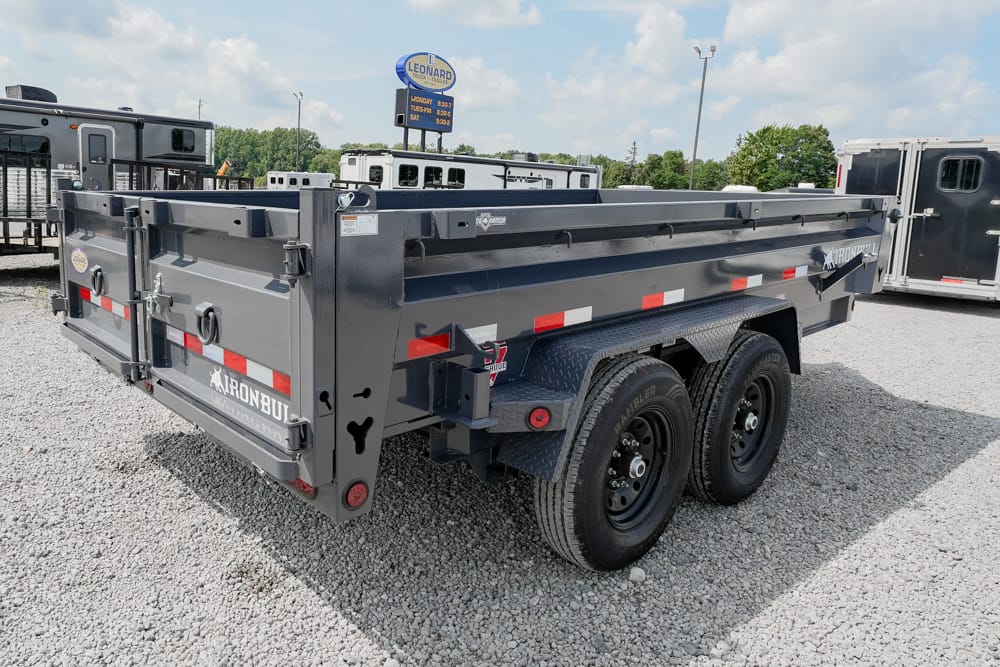 Gray Iron Bull dump trailer with dual rear wheels parked on a gravel lot, side rails raised and reflective strips visible, tailgate closed.