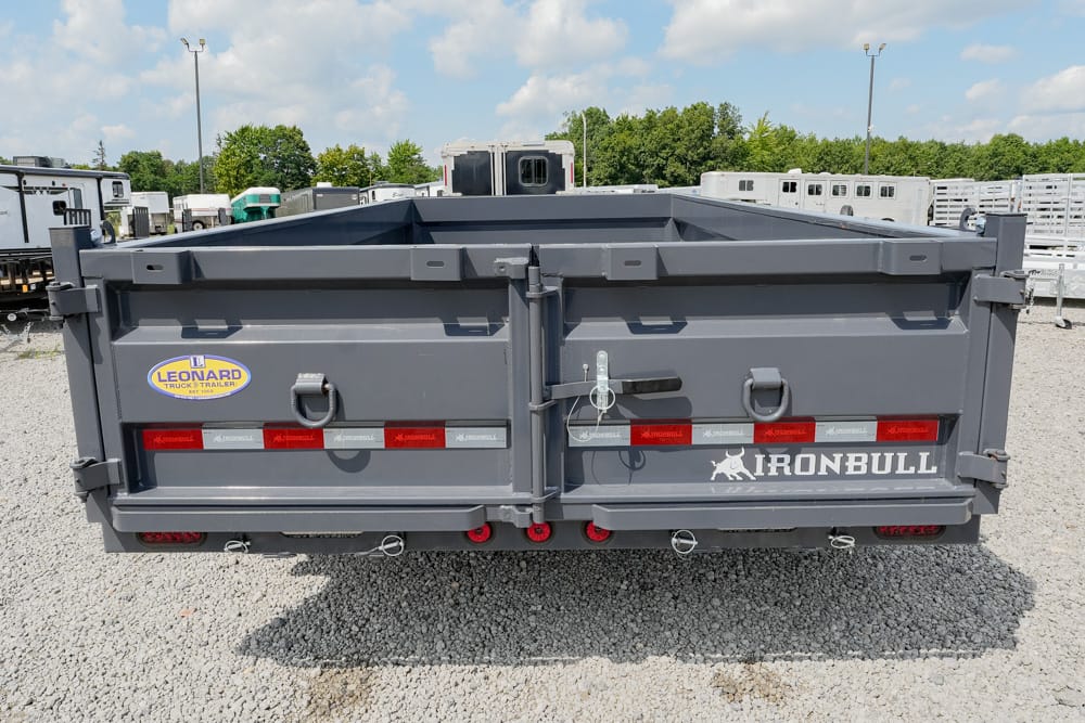 Rear view of a gray Iron Bull dump trailer in a gravel lot, showing taillights, latches, and the Leonard Truck & Trailer logo on the back.