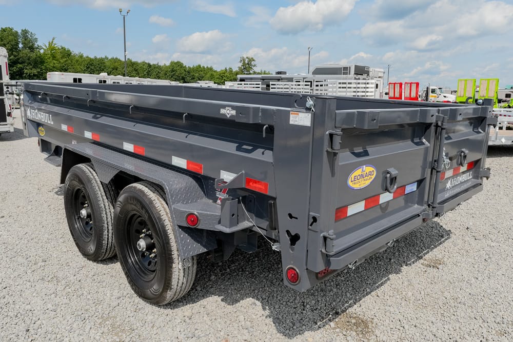 Gray Iron Bull dump trailer with dual axles and rear tailgate, parked on a gravel lot.